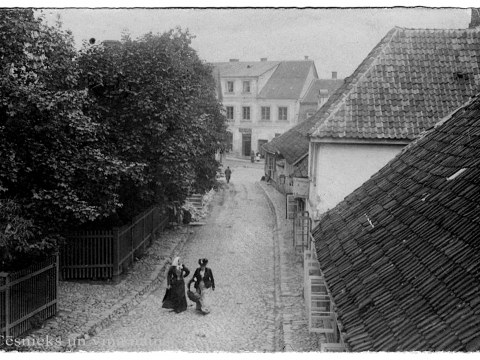 Skats Cēsīs, Lielajā Kalēju ielā. Labajā pusē redzama daļa no divstāvu mūra nama L. Kalēju ielā 3. Diemžēl izkārtnes teksts nav salasāms. Nezināma autora fotogrāfija 20. gs. sākumā. Cēsu muzeja inv. nr. CM 125229.