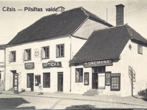 Namā Rīgas ielā 7 atradās Cēsu pilsētas valde, pilsētas aptieka un uzņēmēji: tirgotājs un kurpnieks Ed. Amats, grāmatnieks H. Dreimanis, 20. gs. 30. gadi; CM 63345